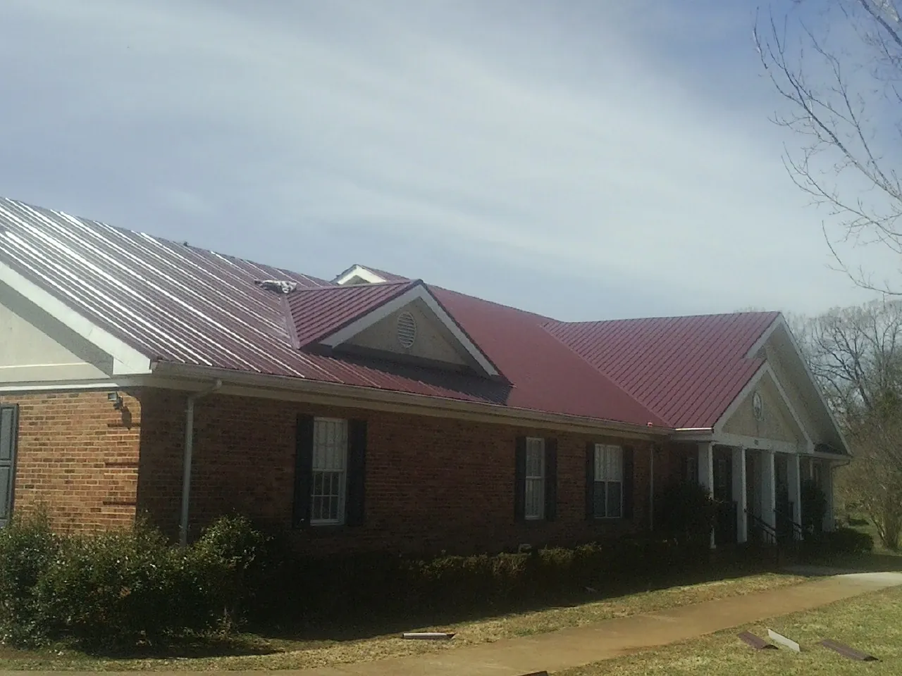 Red metal roof with gabled entries on a long brick building, from a Hail Damage Roof Repair job in Forked River