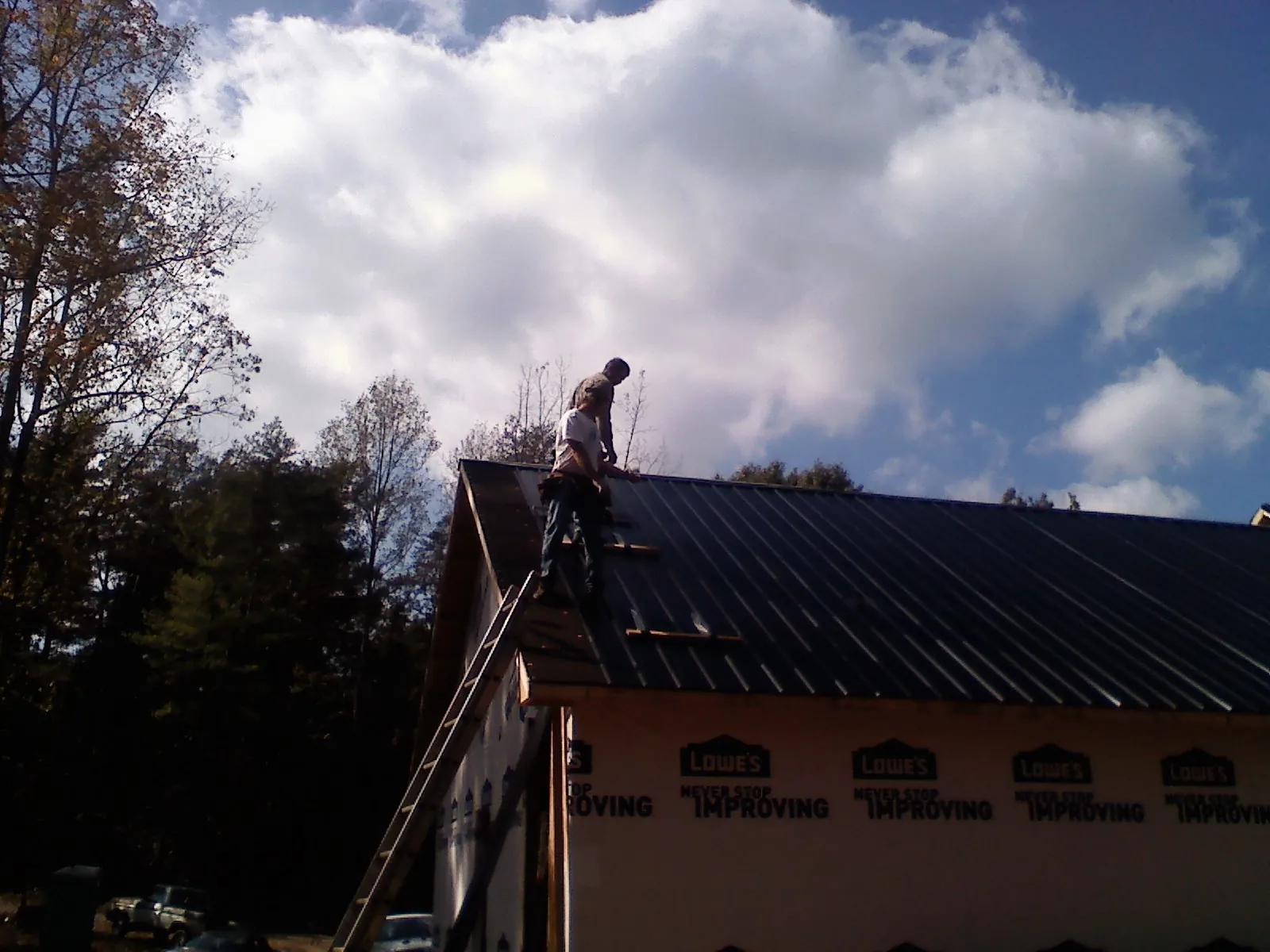 Roofer fastening dark metal panels high against a cloudy sky, from a Roof Inspection job in Forked River